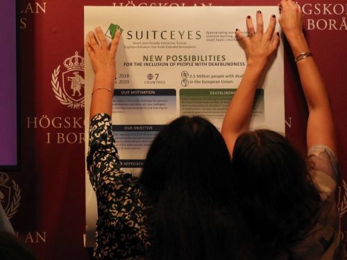 Image of two persons putting up a poster regarding the SUITCEYES project.